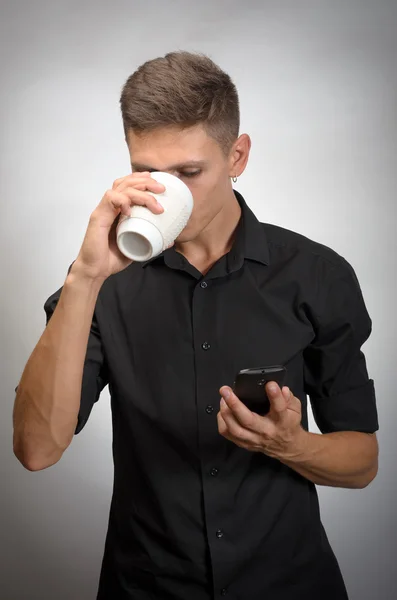Retrato del hombre mira la taza de té de la celebración del teléfono celular — Foto de Stock