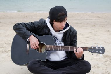 genç adam sahilde gitar çalıyor