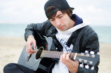 genç adam sahilde gitar çalıyor