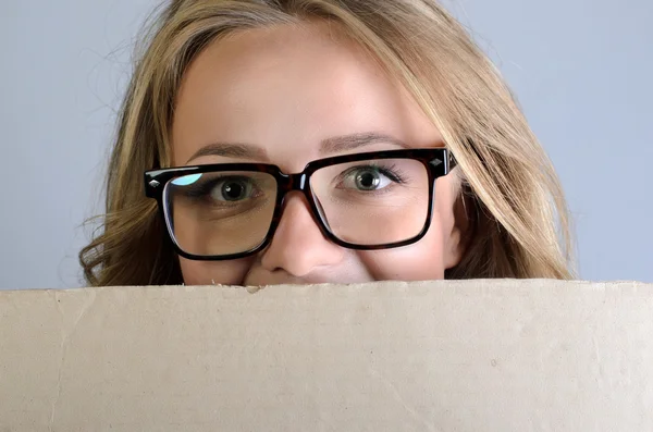 Banner mulher sinal espreitando sobre a borda do outdoor de papel vazio em branco. Mulher bonita com óculos olhando surpreendido e assustado engraçado com olhos abertos largos isolado no fundo da parede cinza — Fotografia de Stock