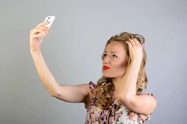 Портрет милої дівчини-підлітка, що знімає власний портрет зі своїм смартфоном на сірому фоні — стокове фото