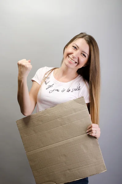 Schöne Frau, die dahinter steht, leere Brettbanner in der Hand, auf grauem Hintergrund — Stockfoto