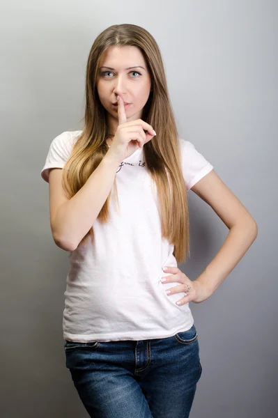 Porträt einer jungen schönen Frau, die vor grauem Hintergrund den Finger auf ihre Lippen legt und um Ruhe bittet — Stockfoto