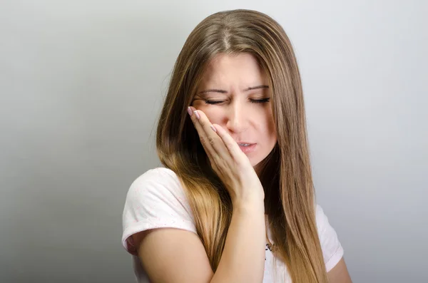 Leiden unter Zahnschmerzen. Schöne junge Frau leidet unter Zahnschmerzen, während sie vor grauem Hintergrund steht — Stockfoto