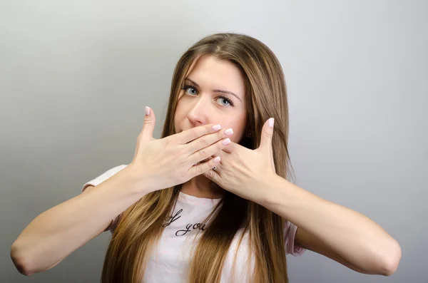 ¡Ups! Mujer joven sorprendida cubriendo la boca con las manos y mirando a la cámara mientras está de pie sobre un fondo gris — Foto de Stock