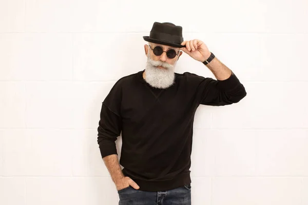 Stylish senior man in dark outfit wearing hat and glasses posing isolated on white background
