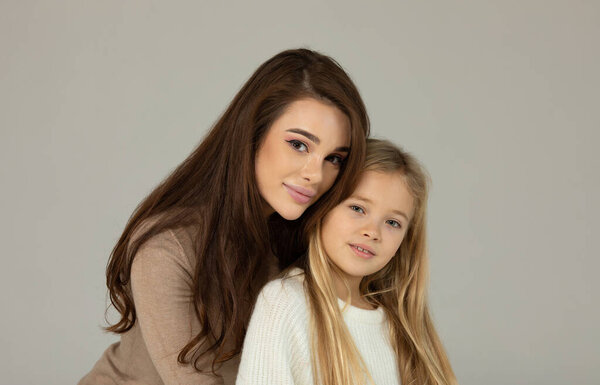 Charming little girl and her beautiful young mom hugging and smiling on grey background. Happy family.