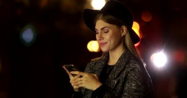 Geceleri açık havada akıllı telefon kullanan şapkalı genç bir kadın.