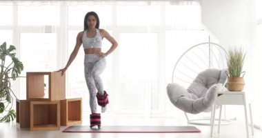 Spor kıyafetli güzel bir kadın. Ayak bileği ağırlığıyla egzersiz yapıyor. Evde covid-19 sırasında ağırlık antrenmanı yapıyor.. 