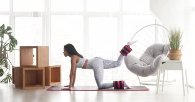 Spor kıyafetli güzel bir kadın. Ayak bileği ağırlığıyla egzersiz yapıyor. Evde covid-19 sırasında ağırlık antrenmanı yapıyor.. 