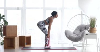 Atletik genç Afrikalı Amerikalı kadın spor yapıyor elastik bantlarla esneme egzersizleri yapıyor, evde antrenman yapıyor. Sağlıklı bir yaşam tarzı. Fitness.