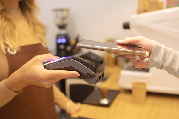 Cropped Shot of Woman Holding Smartphone with Payment Technology Using for Paying for Take Away Coffee in a Cafe.