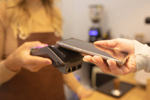 Cropped Shot of Woman Holding Smartphone with Payment Technology Using for Paying for Take Away Coffee in a Cafe.