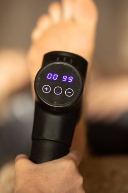 Masaj perküsyon cihazıyla ayak masajı yapan adamın yakın çekim görüntüsü.