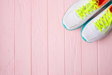 Pembe ahşap arka planda bir çift beyaz spor ayakkabının yakın plan görüntüsü