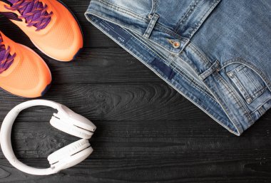 Şık kot pantolonlar, kulaklıklar ve koyu ahşap arka planda turuncu spor ayakkabılar.   