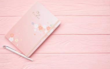 Pembe ahşap arka planda kalemli not defteri.