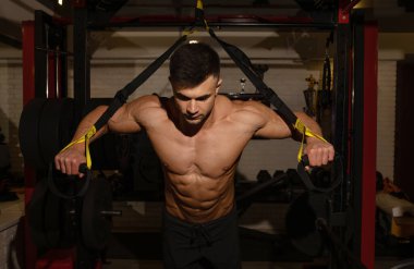 Spor salonunda spor kemerleriyle antrenman yapan kaslı, üstsüz genç adam.