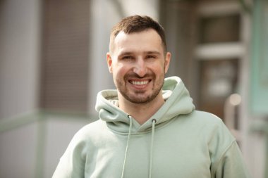 Spor kıyafetli yakışıklı, gülümseyen genç bir adamın açık havada poz verirken portresi.