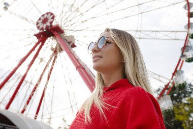 Düşük açılı seksi sarışın kız kırmızı bluzlu ve güneş gözlüklü eğlence parkında. 