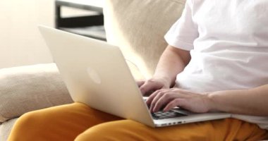 Kapalı alanda dizüstü bilgisayarda daktilo eden genç adamın kırpılmış görüntüsü.