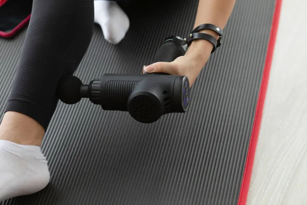 Formda bir kadının evde perküsyon masajcısıyla kaslara masaj yaparken çekilmiş bir fotoğrafı.