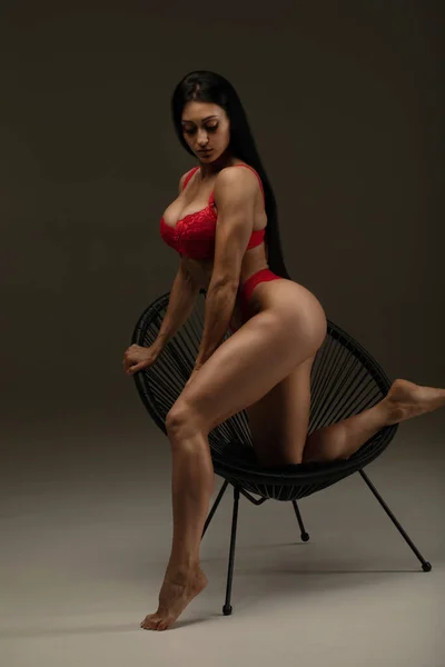 Gri Arka Planda Sandalyede Poz Veren Kırmızı Çamaşırlı Seksi Esmer — Stok fotoğraf