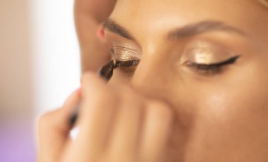 Makyöz, güzellik salonundaki kıza göz kapaklarına oklar çiziyor.