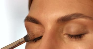 Makyaj sanatçısı genç bir kadının yüzüne makyaj yapıyor.