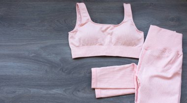 Ahşap bir arka planda fitness eğitimi için pembe spor kıyafetlerinin üst görüntüsü.