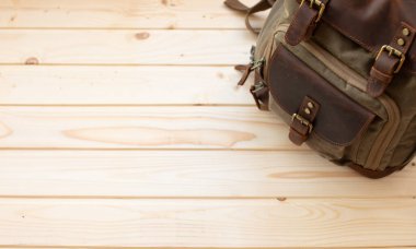 Kahverengi ahşap arka planda fotokopi alanı olan klasik deri sırt çantası.