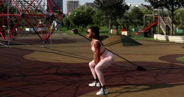 Afrika kökenli Amerikalı genç fitness kadını spor sahasında elastik bantla antrenman yapıyor, açık havada antrenman yapıyor.
