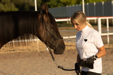 Kız ata binmeye hazırlanıyor, kadın eğitmen bir ata bakıyor..