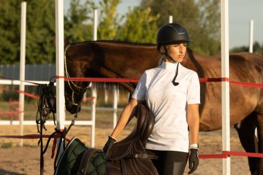 Genç bir kadın ata binmeye hazırlanıyor, eğitmen bir ata bakıyor..