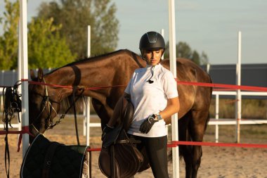 Çekici bir genç kadın ata binmeye hazırlanıyor, eğitmen bir ata bakıyor..