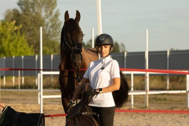 Kız ata binmeye hazırlanıyor, kadın eğitmen bir ata bakıyor..