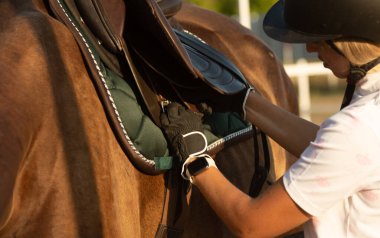 Genç bir kadın ata binmeye hazırlanıyor, eğitmen bir ata bakıyor..