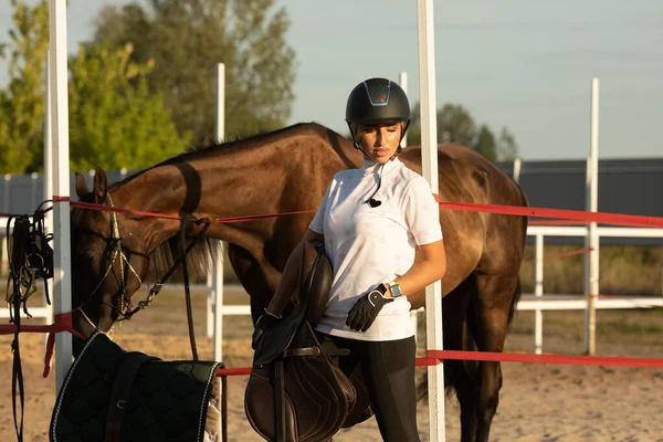 Çekici bir genç kadın ata binmeye hazırlanıyor, eğitmen bir ata bakıyor..