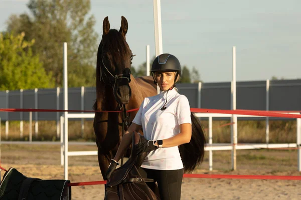 Kız ata binmeye hazırlanıyor, kadın eğitmen bir ata bakıyor..