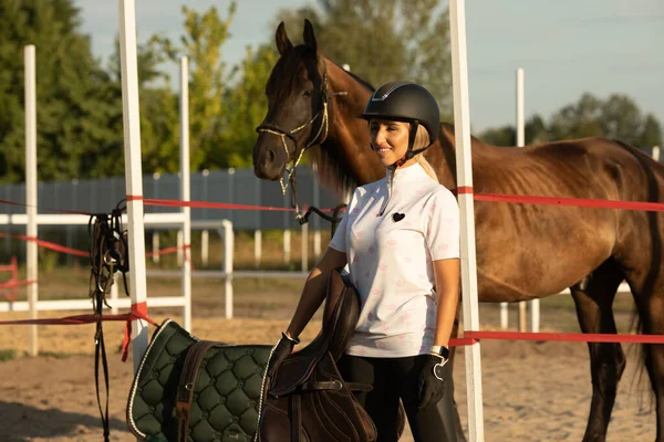 Genç bir kadın ata binmeye hazırlanıyor, eğitmen bir ata bakıyor..