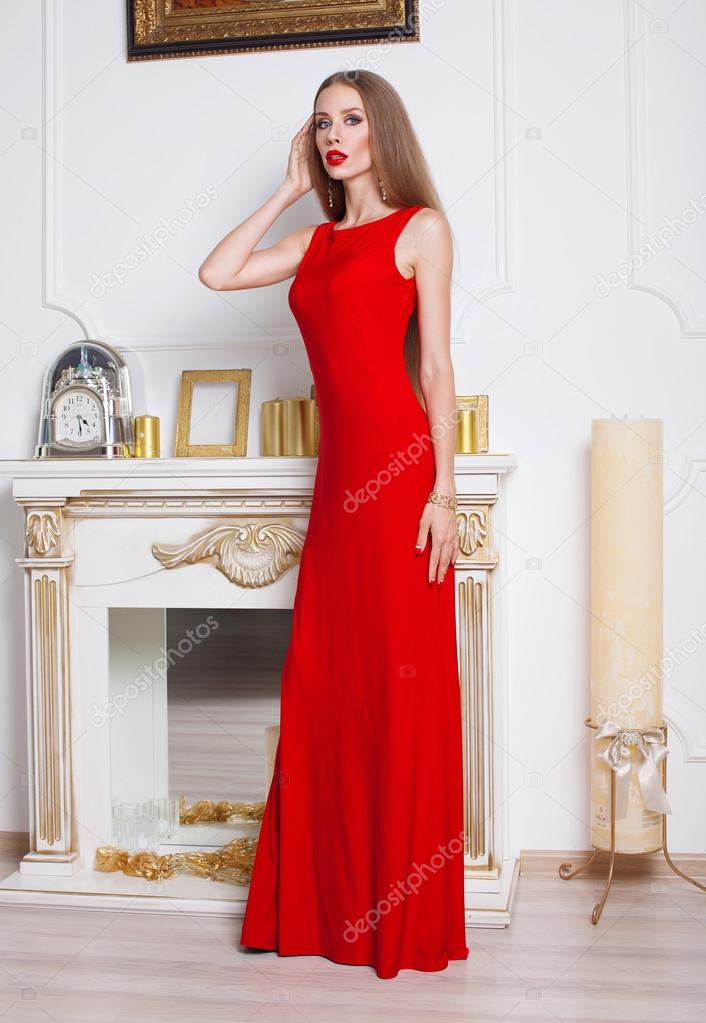 Beautiful sexy young brunette woman with long wavy hair thin slender figure perfect body and pretty face make-up wearing a red evening skinny dress and jewelry