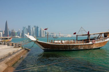 Katar 'daki Doha Corniche, geleneksel dhow tekneleriyle rıhtıma yanaştı ve arka planda şehrin silüeti vardı..