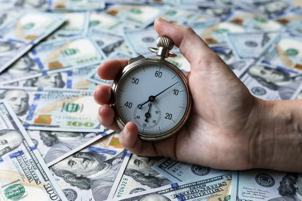 Time is money concept. A stopwatch in a hand on one hundred dollars notes as a background
