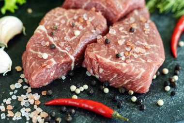 Çiğ mermer et, koyu taş kesme tahtasında baharatlar.