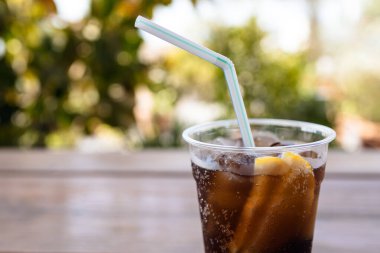 Plastik terli cam, soğuk kola, buz ve arka planda mavi yeşillikler olan iki dilim limon. Boşluğu kopyala.