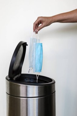 Çöp kutusuna maske atan bir kadın eli.