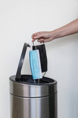 Çöp kutusuna maske atan bir kadın eli.