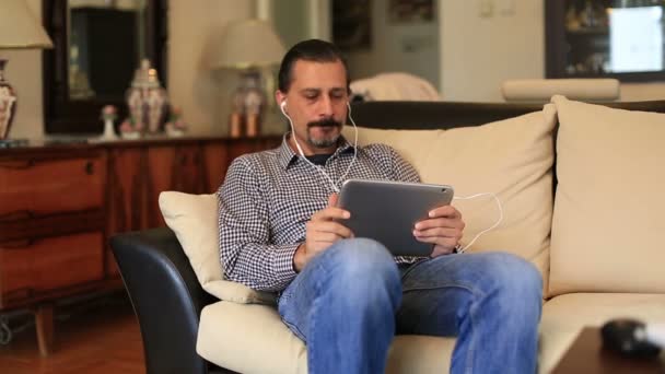 Çekici yakışıklı oturma kanepe ve tablet ile müzik dinleme — Stok video