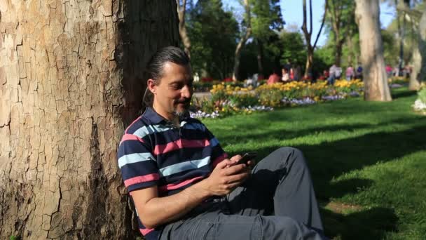 Morena hombre texto masaje celular en parque — Vídeos de Stock