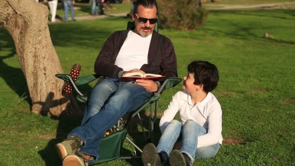 Vader zoon in het park op een zonnige dag lezen — Stockvideo